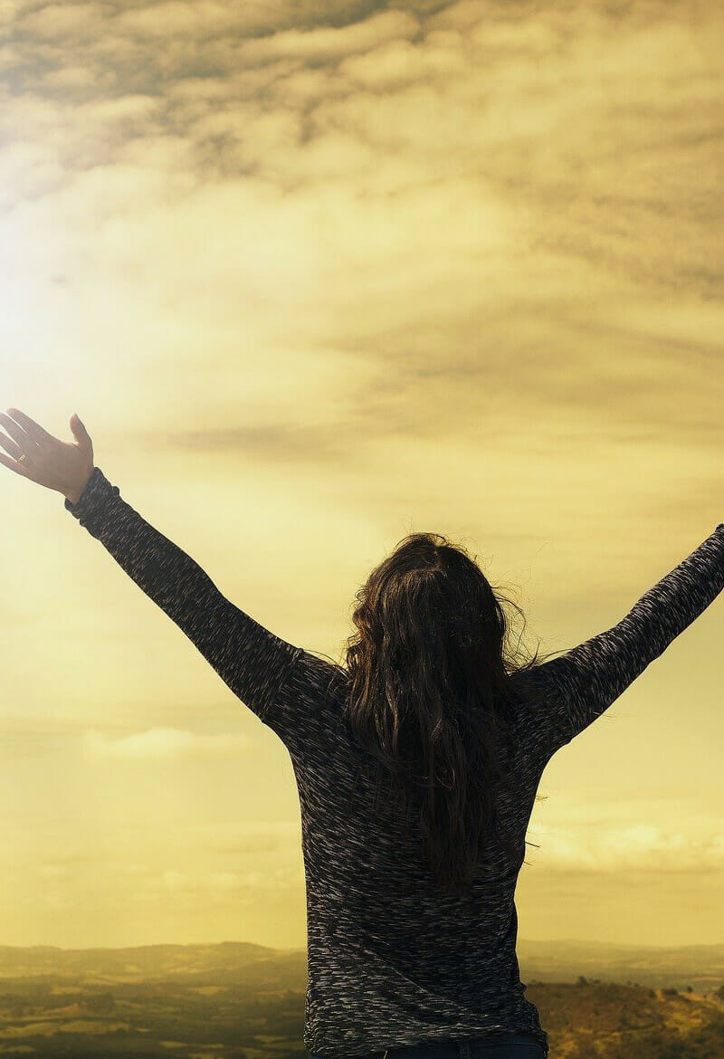 Woman at peace holds her arms up and embraces the sun