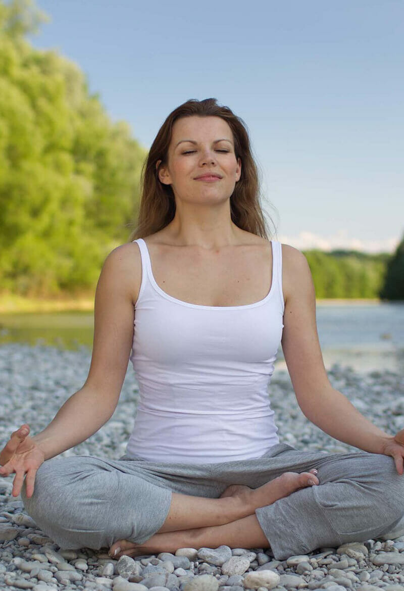 Woman performs yoga on rocks by a lake