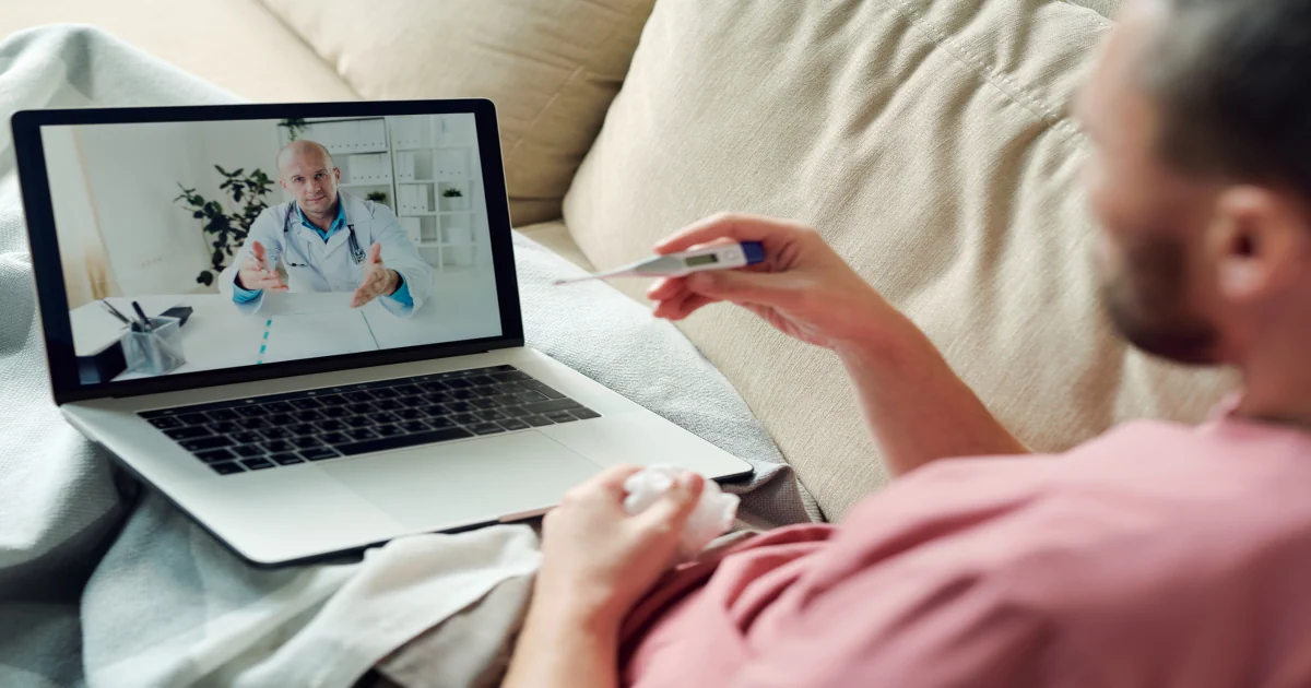 Man holding a thermometer during a telehealth urgent care visit with his provider Solstice Health & Wellness Sarasota FL Man holding a thermometer during a telehealth urgent care visit with his provider Solstice Health & Wellness Sarasota FL
