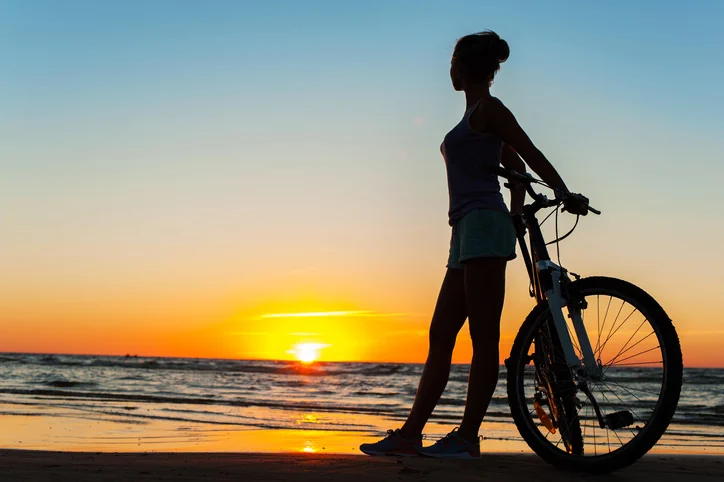 Woman with bike enjoying the moment and grateful for integrative addiction treatment lifestyle wellness activities and watching the sunset